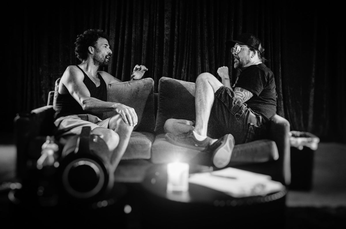 Black and white backstage photo of Jon Theodore and Dave Grohl talking on a couch in Nashville, a candle on the table in front, by Andreas Neumann